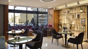 En moderne hotellobby med et siddeområde, en bogreol og store vinduer med udsigt over byen.