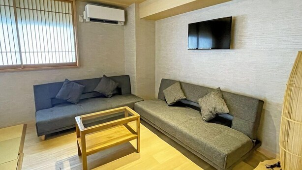 A living room with two sofas, a coffee table, a TV mounted on the wall, and an air conditioning unit. - Stay Sakura Tokyo (Tokyo)