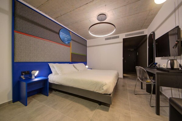 A modern bedroom with a bed, bedside table, desk, and chair. - Ikyk Hotel (St. Julian's)