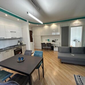 Una cocina moderna con armarios blancos, una mesa de comedor con sillas y un sofá gris en la sala de estar.