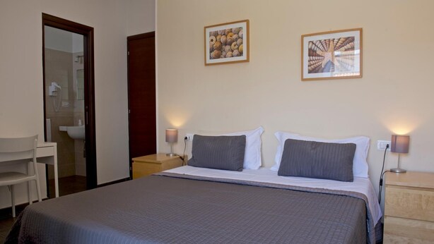 A hotel room with a large bed, two bedside tables with lamps, a desk with a chair, and two framed pictures on the wall. - Hotel Centosedici (Terracina)
