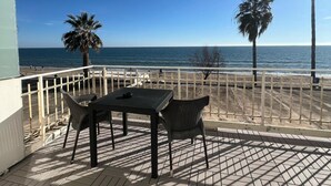 A patio with a table and chairs overlooking a beach with palm trees and the ocean. - Hotel Centosedici (Terracina)