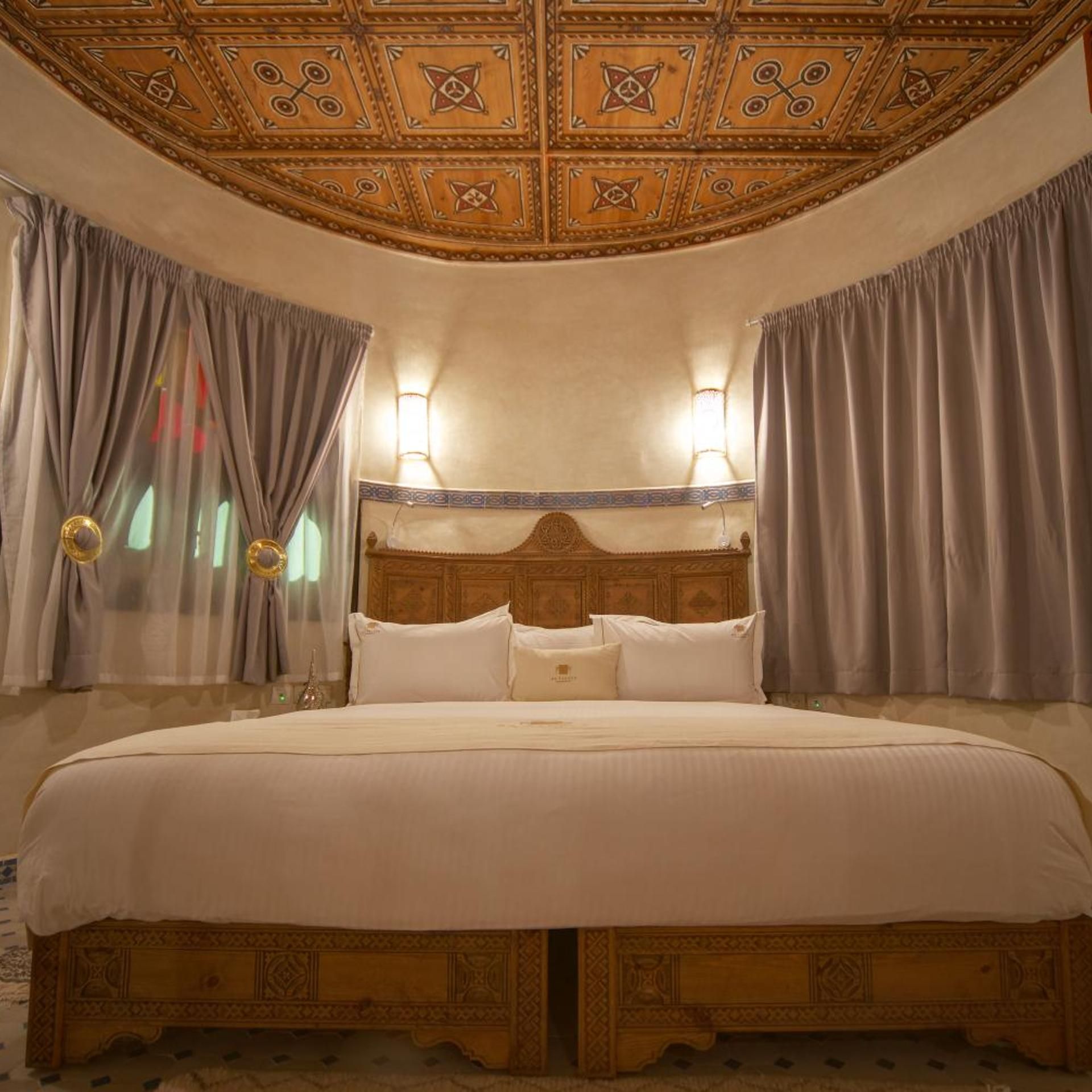 A hotel room with a large bed, a wooden headboard, and a decorative ceiling.