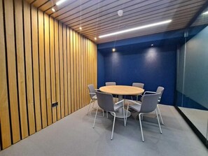 Un salón de conferencias con una mesa redonda, seis sillas, paneles de madera y paredes con detalles azules.