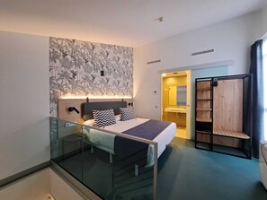 Ein modernes Hotelzimmer mit Bett, Glastrennwand, Holzschrank und sichtbarem Badezimmer durch eine geöffnete Tür.