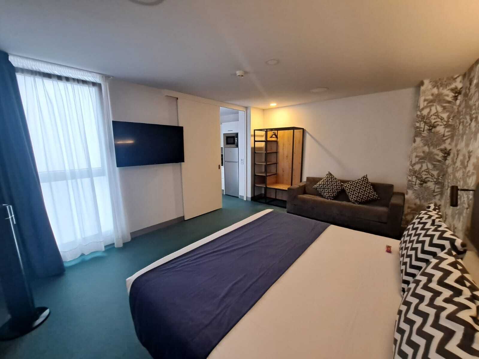 Una habitación de hotel con cama, sofá, televisión, armario y kitchenette.
