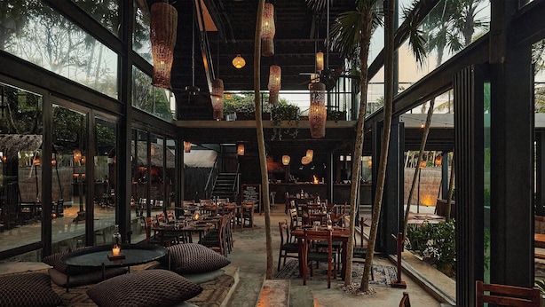 An indoor dining area with tables and chairs, hanging lights, and large windows. - Our Habitas Tulum (Tulum)