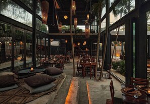 Un espace de restauration intérieur avec des tables et des chaises, des luminaires suspendus et de grandes fenêtres.