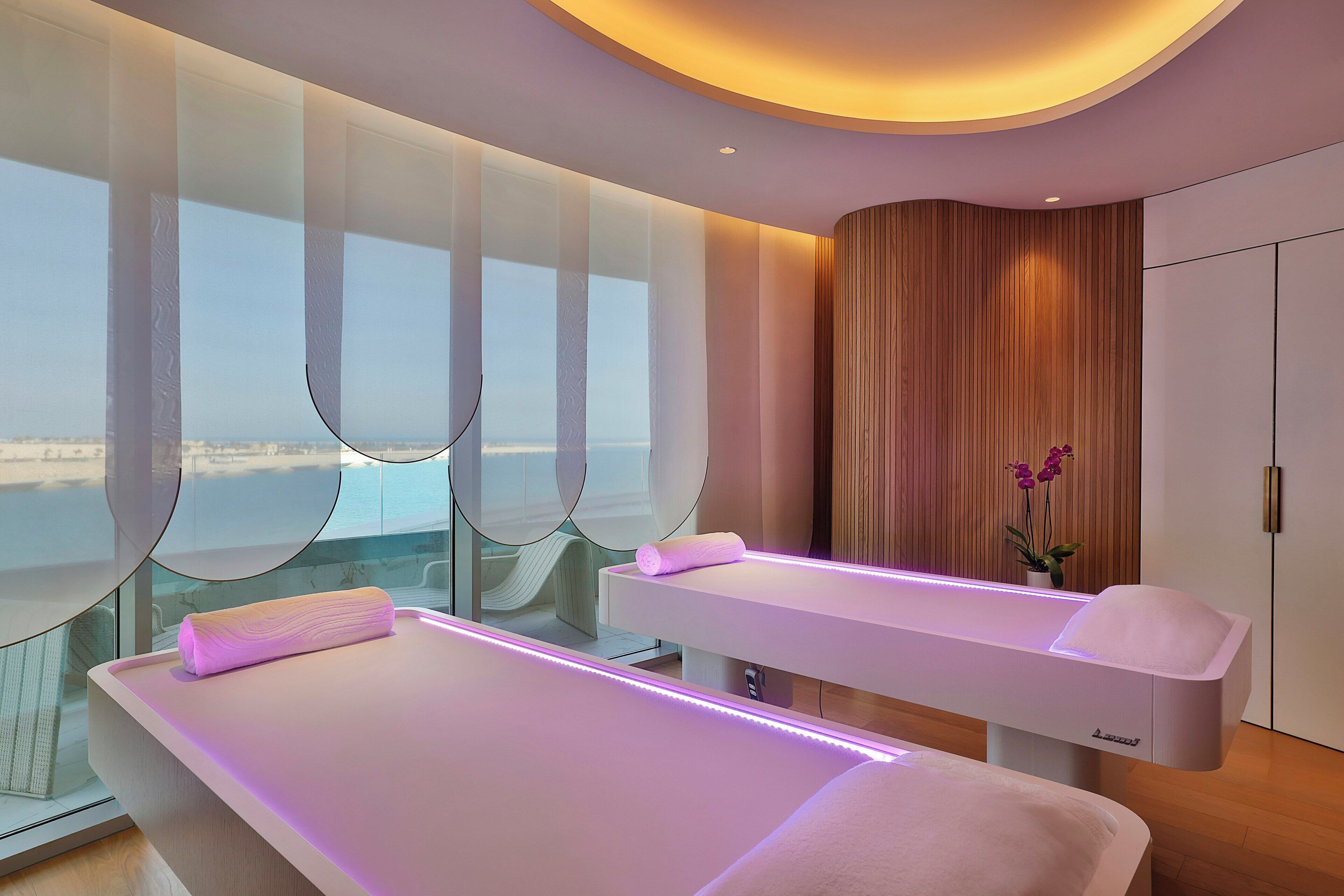 A modern spa room with two treatment beds, large windows, and a view of the sea.