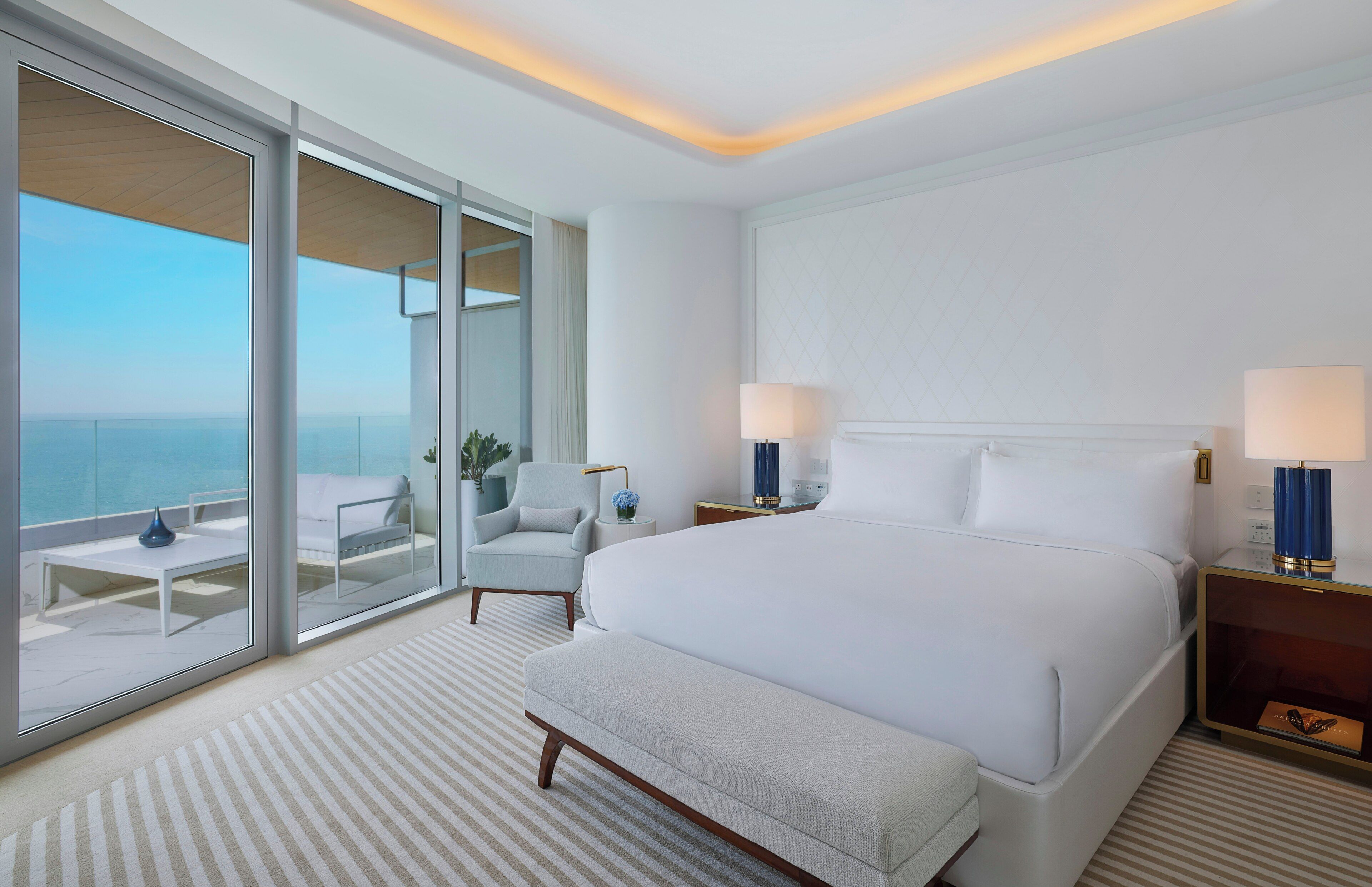 Una habitación de hotel moderna con una cama grande, un área de descanso con vistas y un balcón.