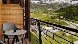 Een balkon met houten vloer, twee stoelen en een tafel. In de verte is een bergtop te zien.
