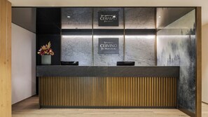 A reception desk with two signs, a wooden slat wall, and a potted plant. - Vretreats Cervino The Alps (Valtournenche)