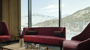 Een kamer met een rode bank, twee fauteuils, een salontafel en een groot raam met uitzicht op een besneeuwde berg.
