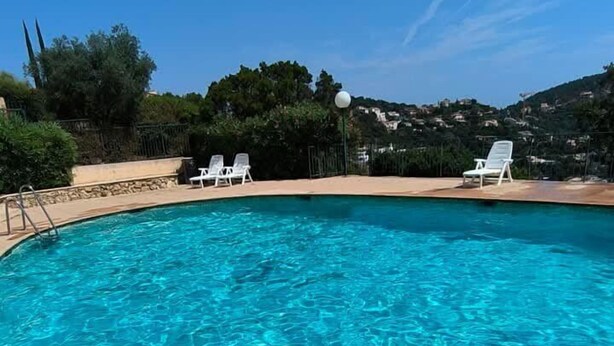 Una piscina azul cristalina con sillas de descanso blancas y una terraza de piedra.