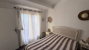 Un dormitorio con cama, mesita de noche, sombrero colgado en la pared y una puerta con cortinas.