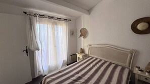 Ein Schlafzimmer mit einem Bett, einem Nachttisch, einem an der Wand befestigten Hut und einer Tür mit Vorhängen.