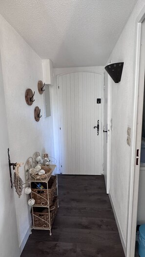 Ein Flur mit einer weißen Tür, einer Wandleuchte und einem Metallregal mit Körben und Dekoration.