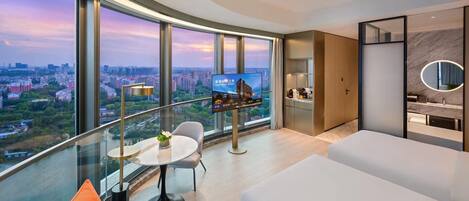 A modern hotel room with a curved balcony, a TV screen, a dining area, and a bathroom with a marble vanity.
