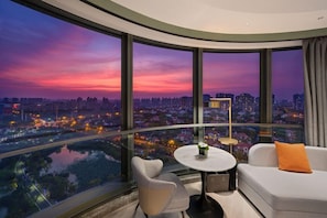 A modern room with a curved glass wall offering a city view at dusk. - Novotel Shanghai Caohejing (Shanghai)