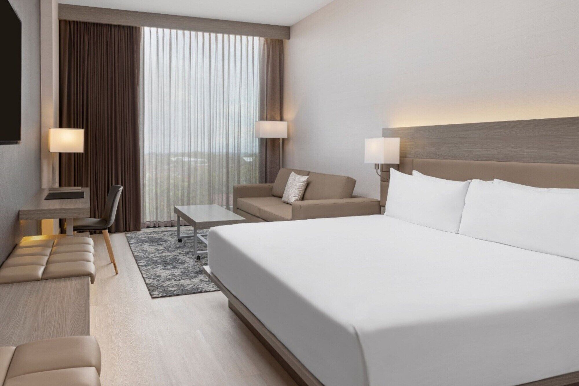 Quarto de hotel moderno com uma cama grande, um sofá, uma escrivaninha e duas luminárias.