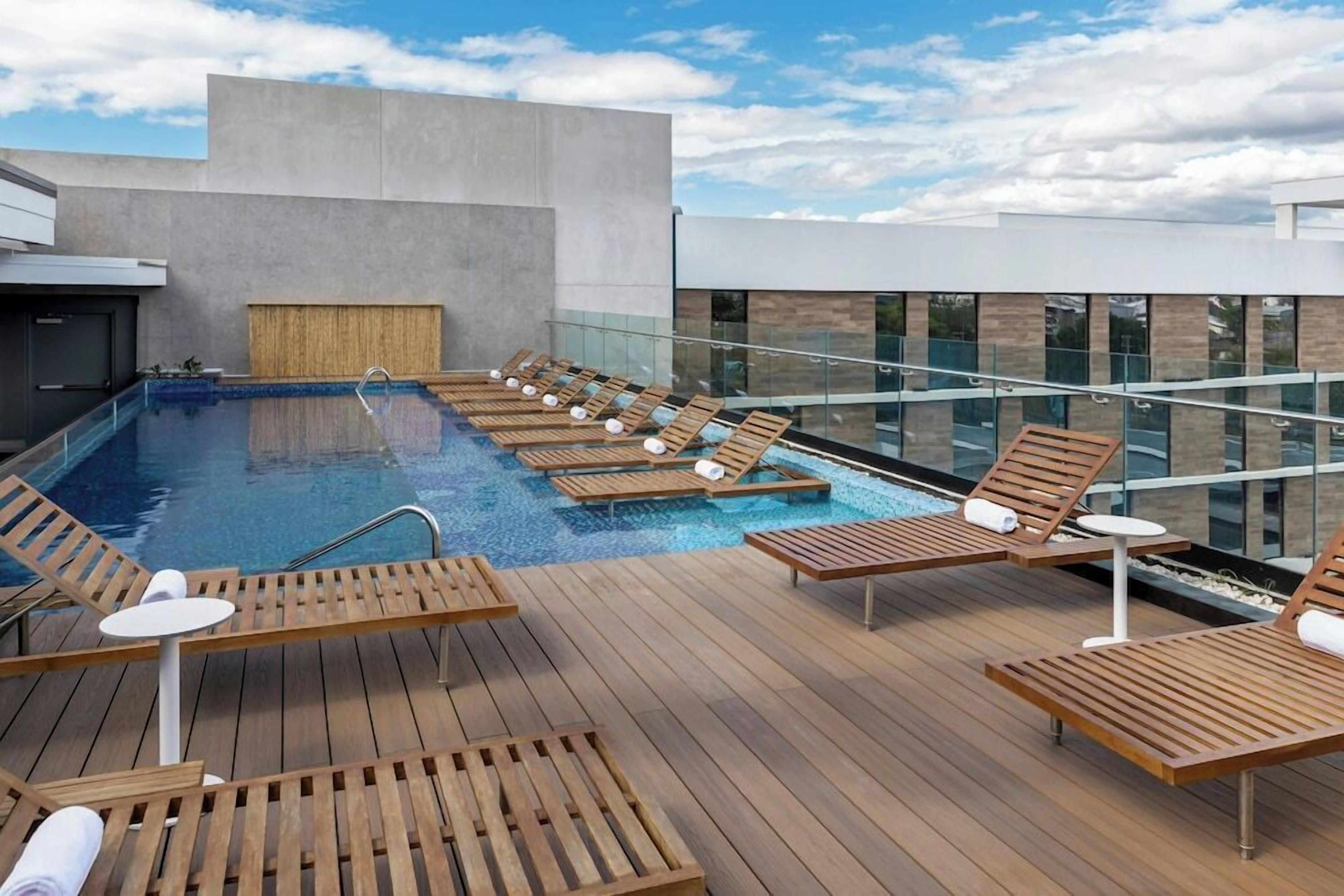 A rooftop pool area with wooden loungers and a glass railing.