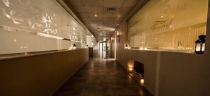 Un couloir avec un long comptoir d’accueil, des panneaux muraux décoratifs et une ambiance chaleureuse et accueillante, rehaussée par un éclairage doux.