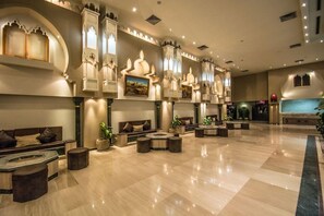 Eine großzügige Lobby mit poliertem Marmorboden, Sitzbereichen mit Sofas und runden Tischen sowie dekorativen Wandleuchten.