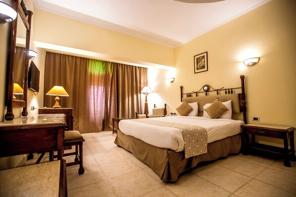 A hotel room with a large bed, a desk, and a chair. There are two lamps on the desk and a mirror on the wall. - Sunny Days Palma De Mirette Resort (Hurghada)