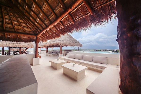 A beachside lounge with thatched roofs, white cushioned seating, and a view of the ocean.