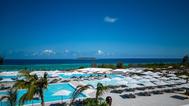 A resort with multiple swimming pools, lounge chairs, and umbrellas, overlooking a clear blue sea and a distant island. - The Mora Zanzibar (Matemwe)