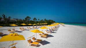 A beach with rows of sun loungers and yellow umbrellas, a clear blue sky, and a calm sea. - The Mora Zanzibar (Matemwe)