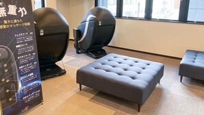 A room with two massage chairs, a large flat-screen TV, and a window with a city view.