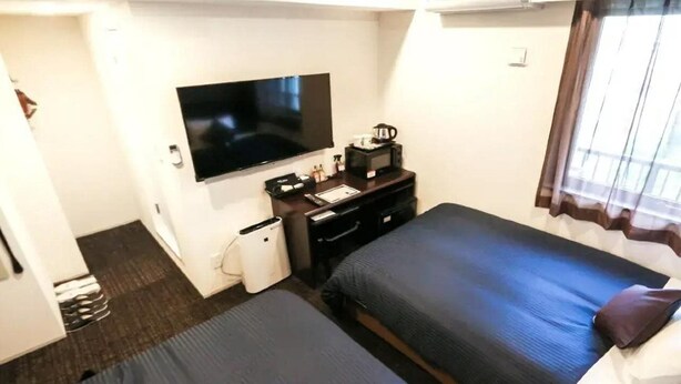 A hotel room with a bed, a TV, a desk with a computer, and a window with curtains.