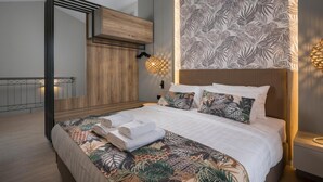 A modern bedroom with a large bed, a wooden headboard, a patterned wall, and a balcony with a railing. - Mare Blue and Suites (Apokoronas)