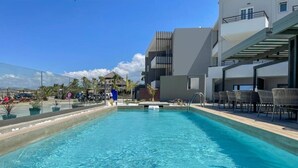 A swimming pool with lounge chairs and a modern building in the background. - Mare Blue and Suites (Apokoronas)
