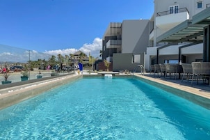 Una piscina con sillas de descanso y un edificio moderno al fondo.
