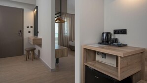 A modern hotel room with a wooden desk, a built-in coffee machine, a mini-fridge, and a hanging light fixture. - Mare Blue and Suites (Apokoronas)