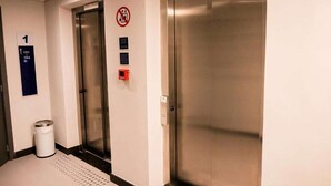 Εσωτερικός χώρος ανελκυστήρα με μεταλλική επένδυση, κάδος απορριμμάτων και σήμα απαγόρευσης καπνίσματος.