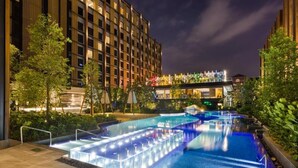 Un hôtel moderne doté d’une vaste piscine extérieure, entourée de verdure et éclairée par un système d’éclairage d’ambiance.