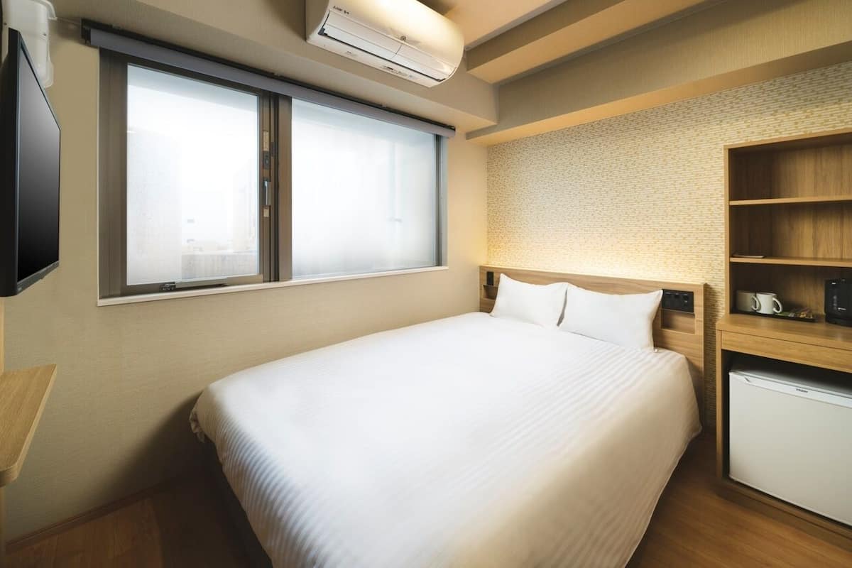 A hotel room with a bed, a television, a mini-fridge, and a shelf with a coffee maker.