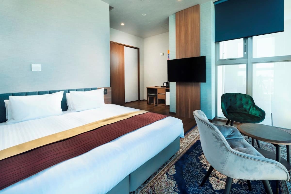 A hotel room with a bed, a desk, a TV, a chair, and large windows.