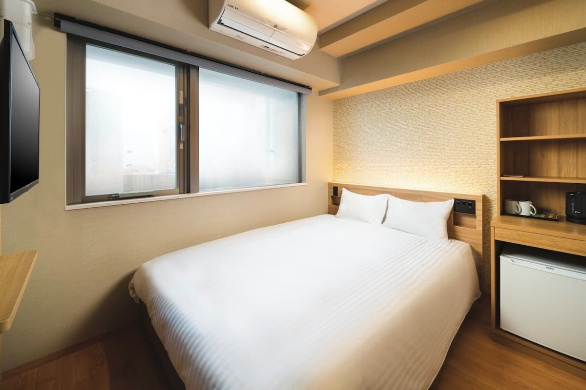 A hotel room with a bed, a television, a small kitchenette, and a window.