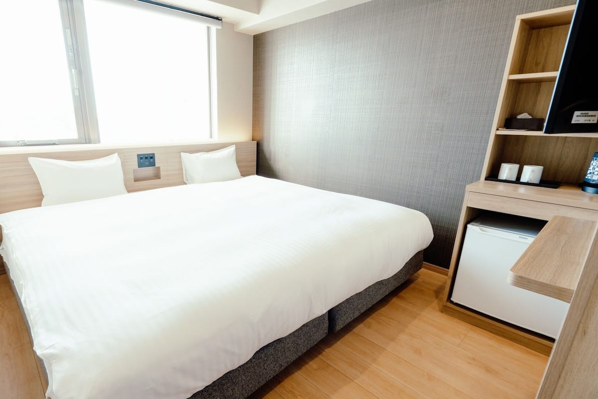 A hotel room with a bed, a desk, a chair, and a small kitchenette.