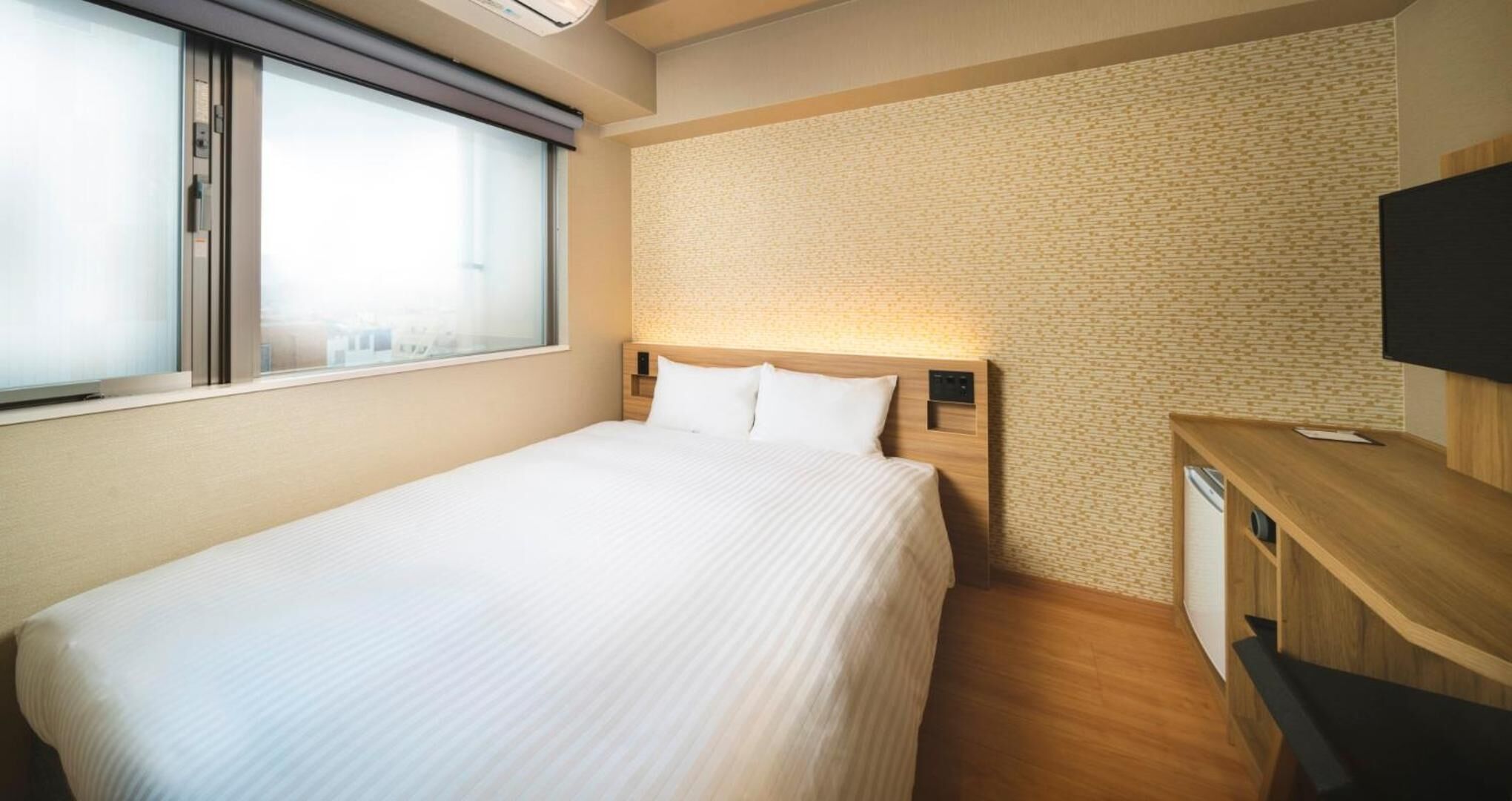 A hotel room with a large bed, a wooden headboard, a flat-screen TV, and a small desk.