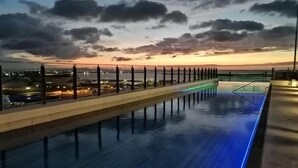 Une piscine sur le toit offrant une vue sur les gratte-ciel de la ville au coucher du soleil.