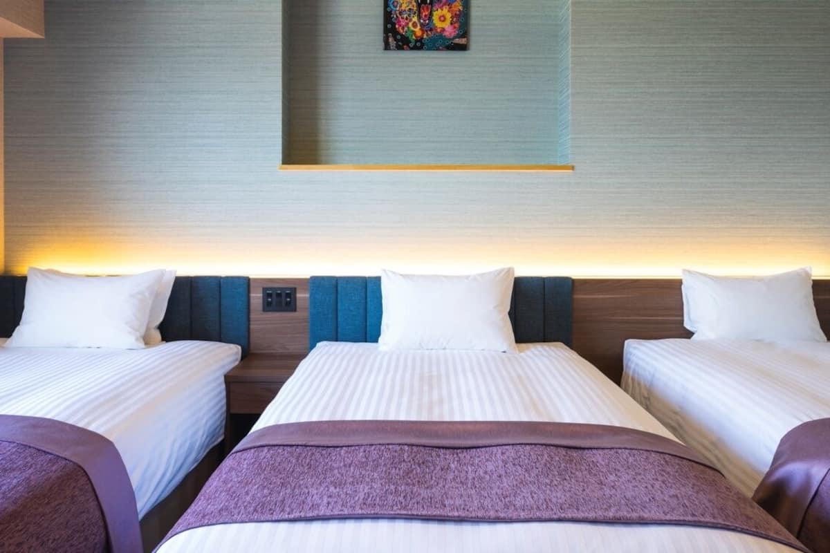 A hotel room with three beds, a wall-mounted artwork, and a recessed ceiling light.