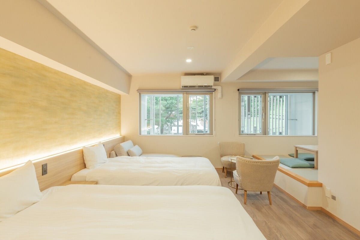 A hotel room with two beds, a desk, a chair, and large windows.