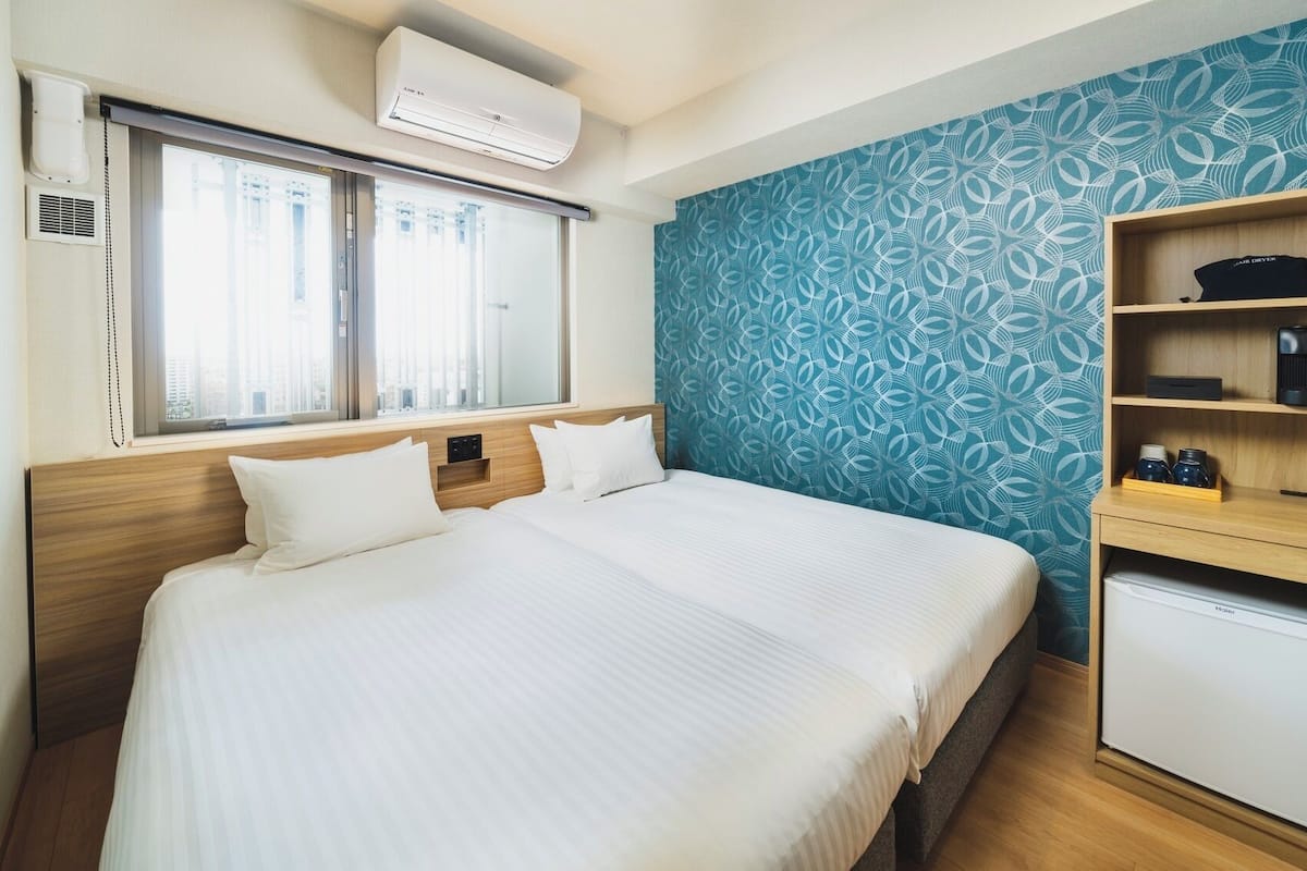 A hotel room with a bed, a small desk, a heater, and a window with blinds.