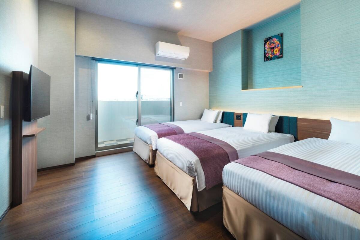 A hotel room with two beds, a TV, an air conditioning unit, and a painting on the wall.