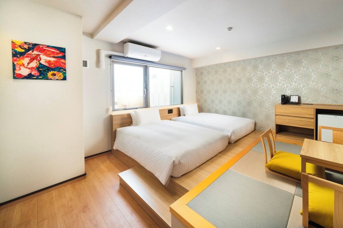 A hotel room with a bed, a desk, a chair, a window, and an air conditioning unit.